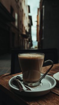 A warm coffee cup on a wooden table in a quaint urban alleyway.