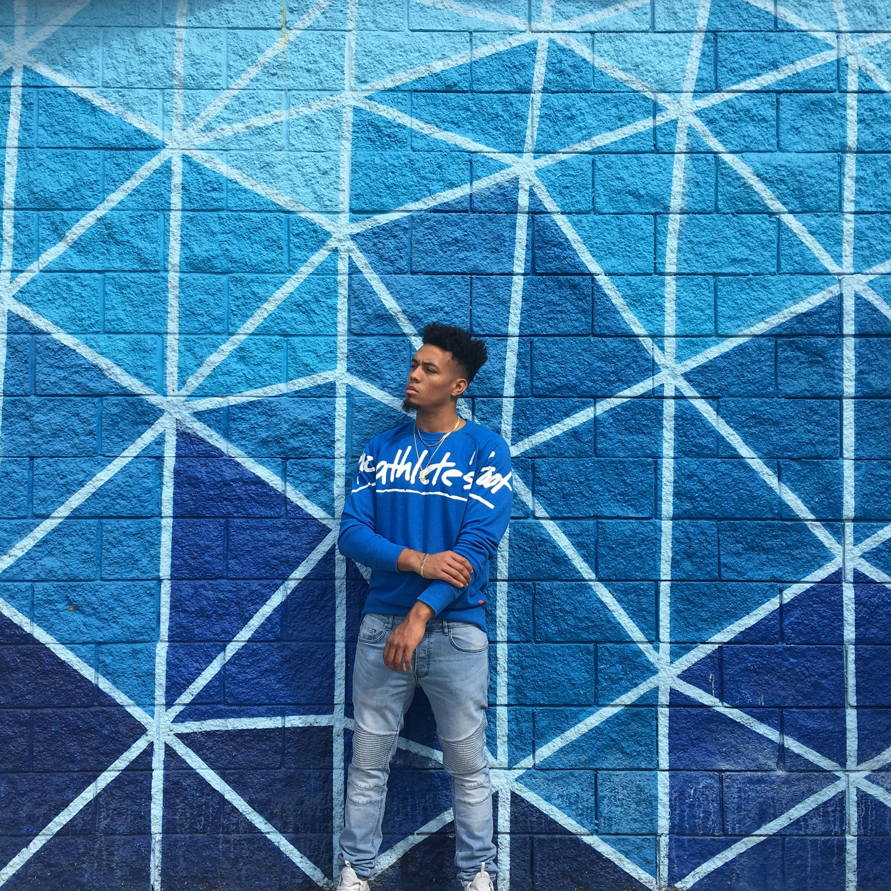A fashionable man in blue attire stands against a striking geometric wall in Atlanta, GA.