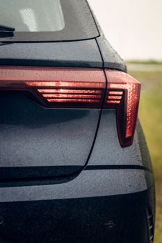 Detailed close-up of a car's tail light covered in rain droplets, showcasing its sleek design.