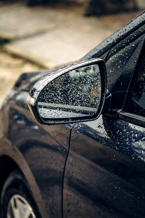 A car is shown in the rain with its side mirror