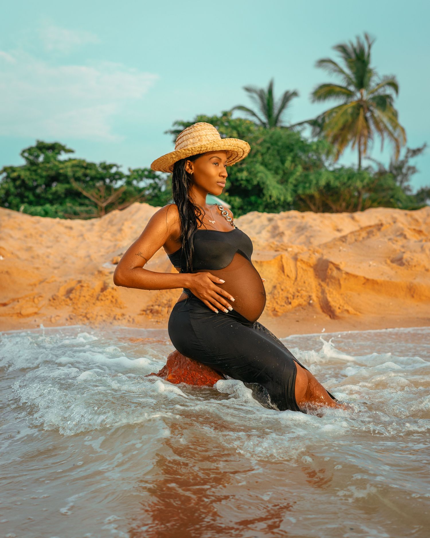 Future maman portant une robe légère et un chapeau au bord de la mer