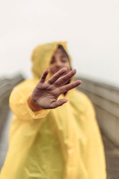 Woman raising hand in yellow raincoat on a misty day at Ilha Comprida, Brasil.