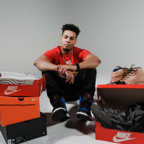 Man in Red Crew-neck T-shirt Sitting Beside Nike Shoe Boxes