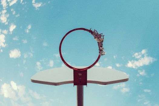A worn basketball hoop under a bright blue summer sky, showcasing urban recreation charm.