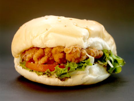 Delicious close-up of a classic burger featuring crispy fried chicken, fresh lettuce, and tomato in a sesame seed bun.