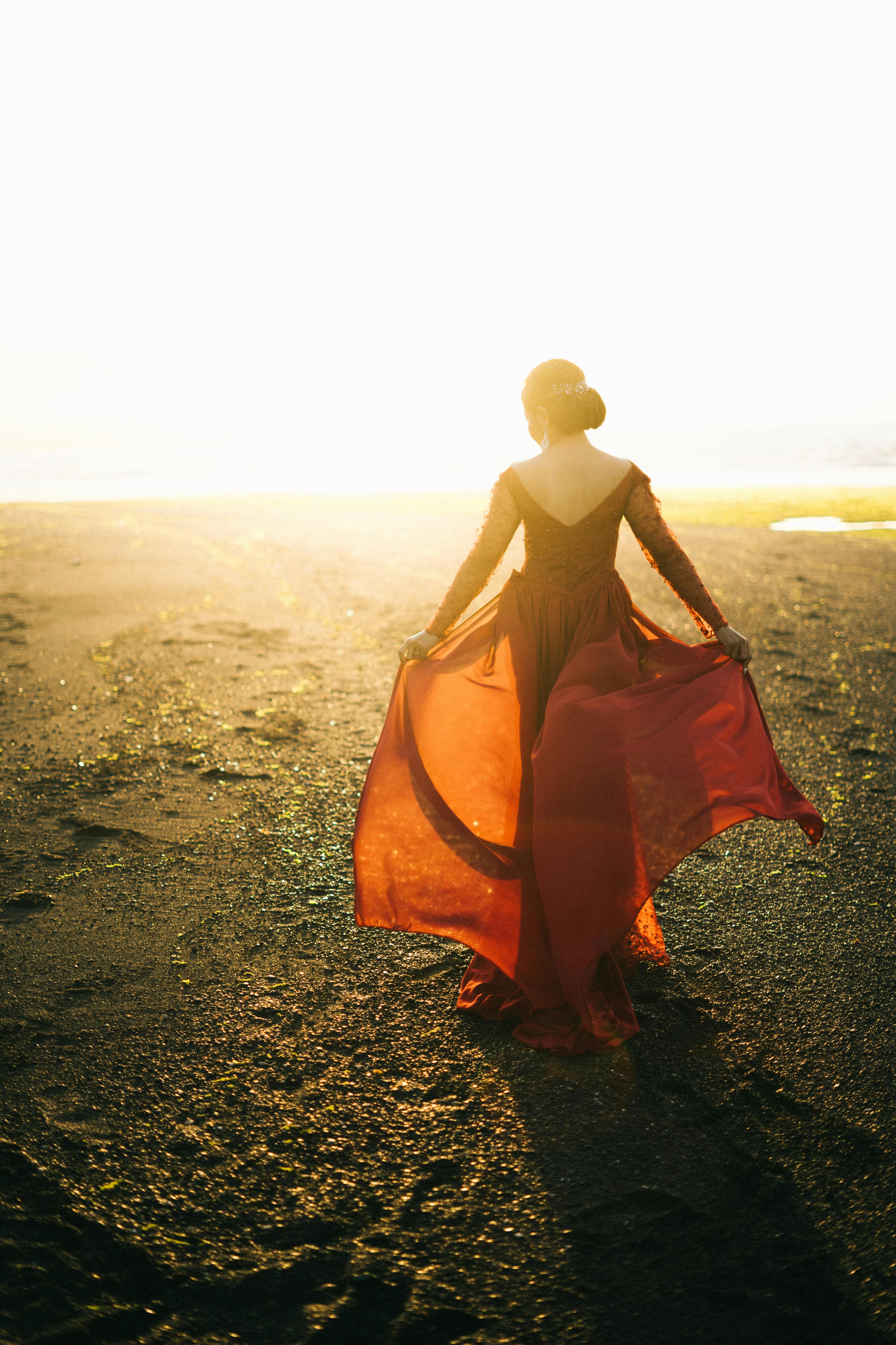 一名女子身穿飘逸的红色连衣裙，优雅地走在阳光明媚的海滩上