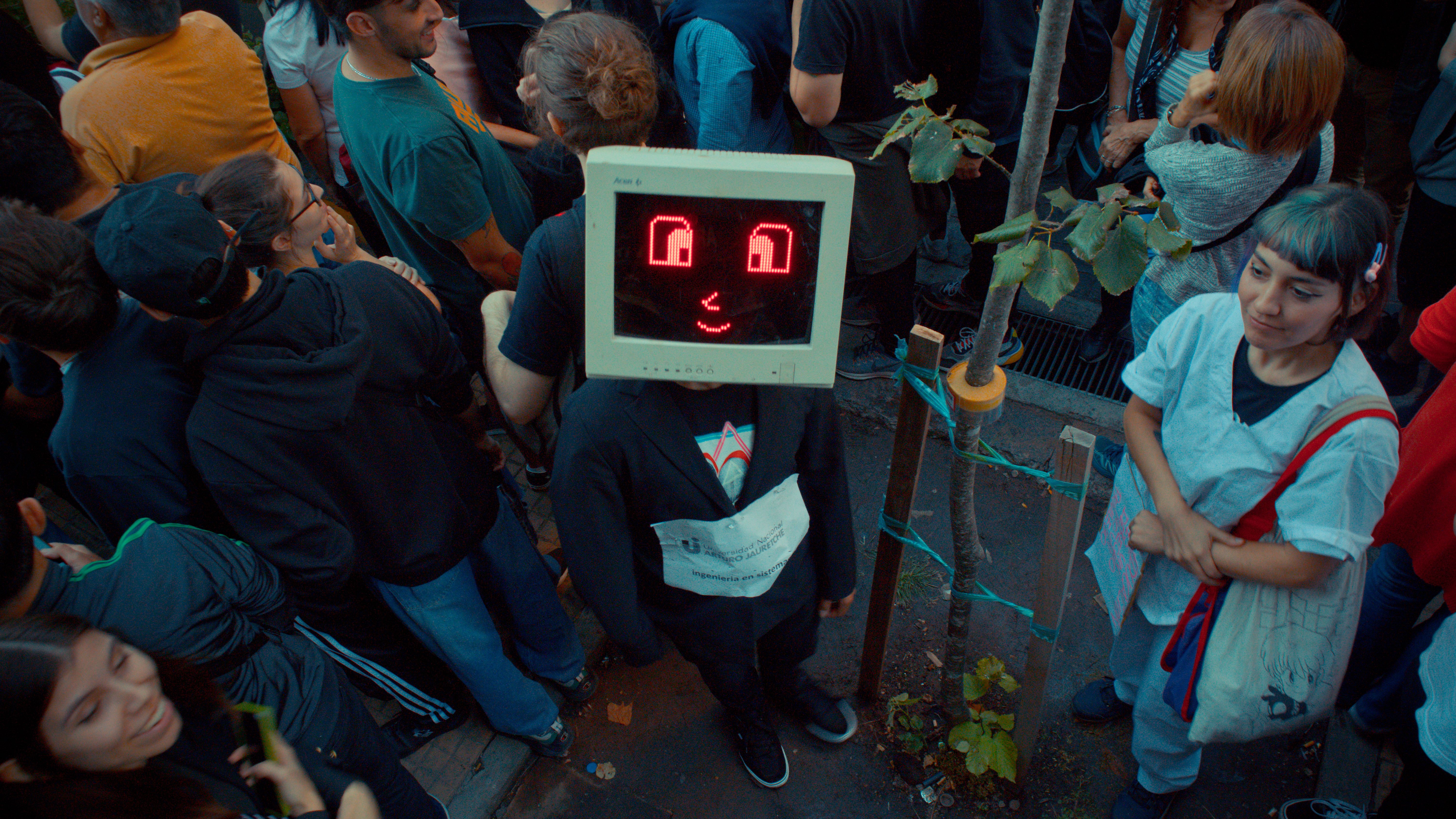 Unique character with a monitor mask amidst a lively crowd during a street event.