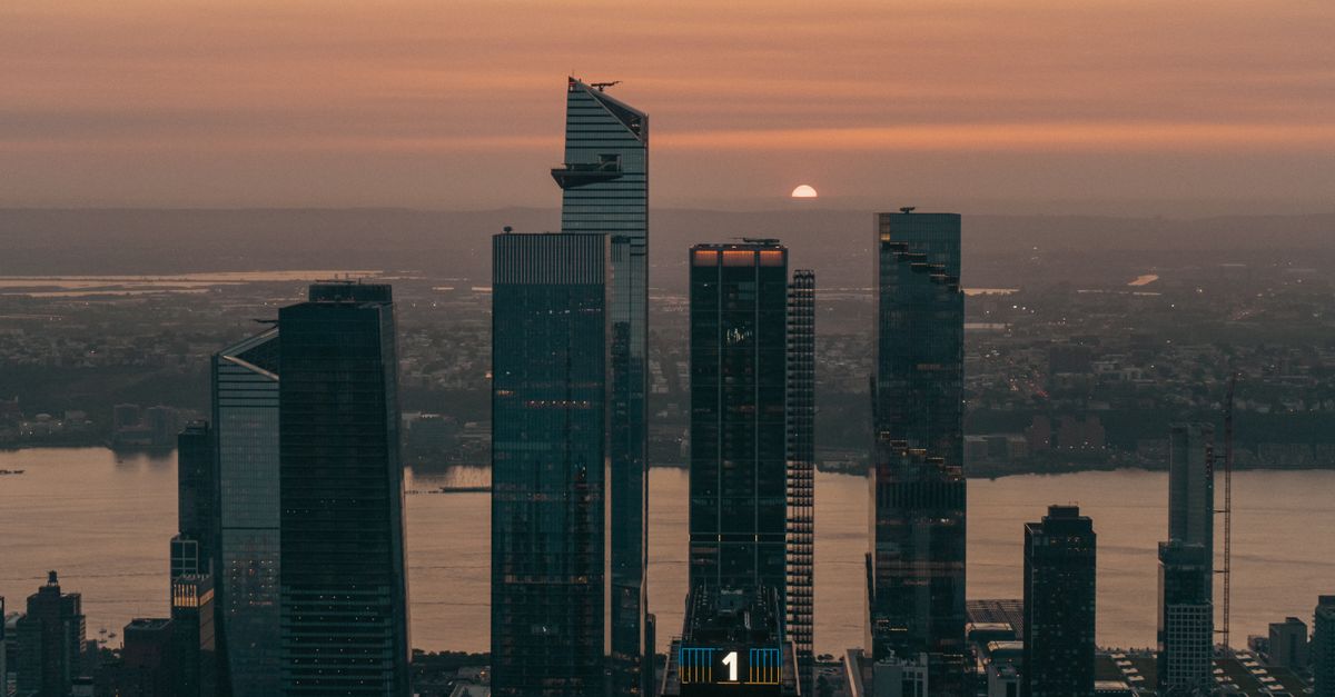 Dramatic sunset view of New York City skyscrapers with the sun setting on the horizon.