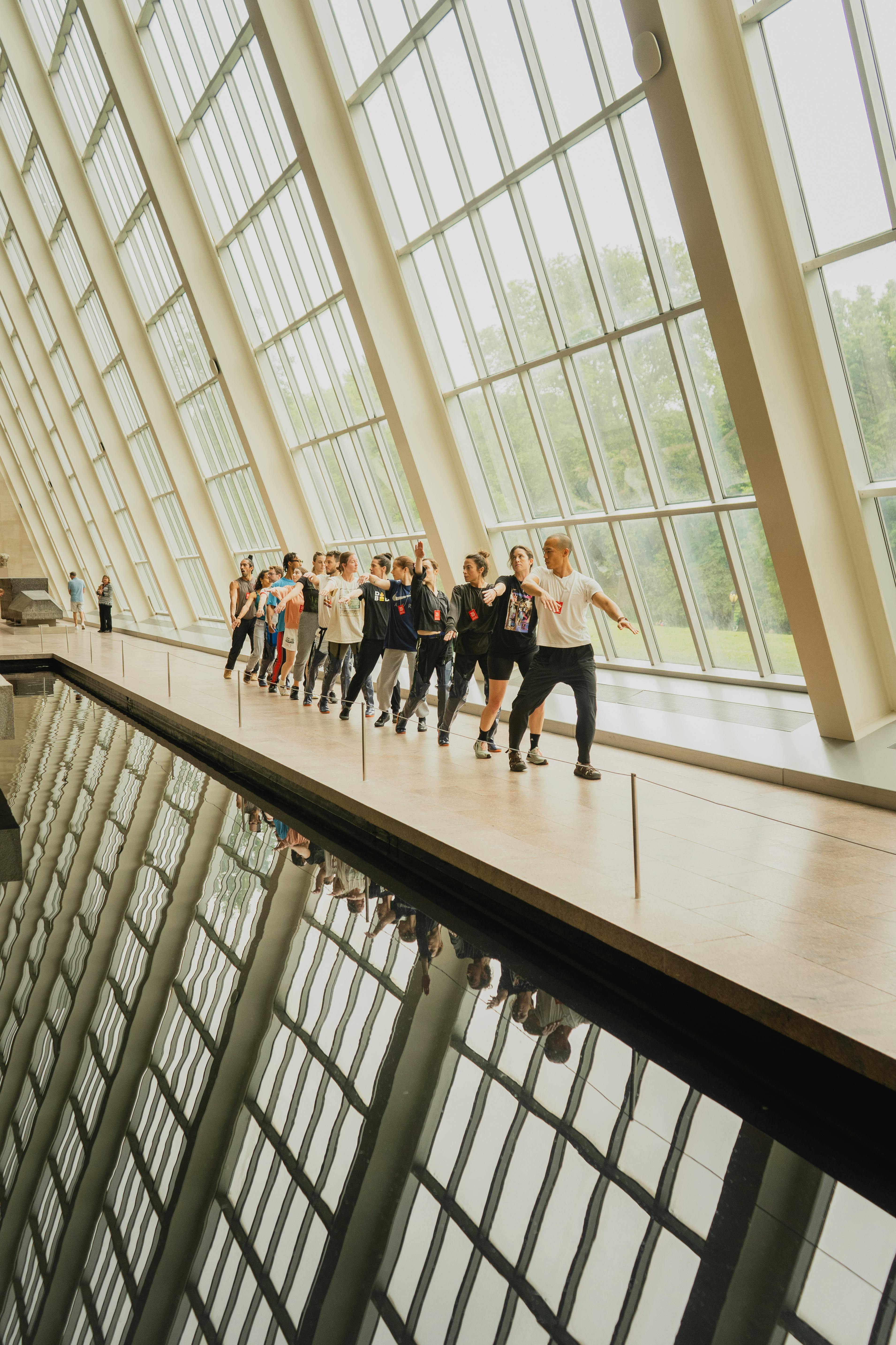 Group of people walking along a windowed corridor with reflections, showcasing modern architecture in a museum.