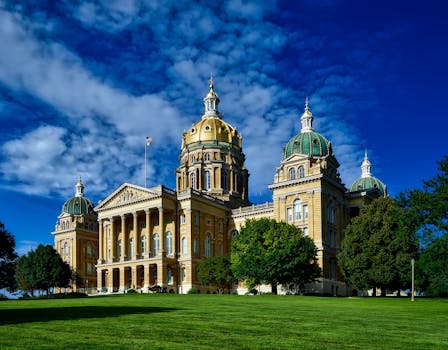 Majestic Iowa State Capitol with golden dome and lush green lawn on a clear sunny day.