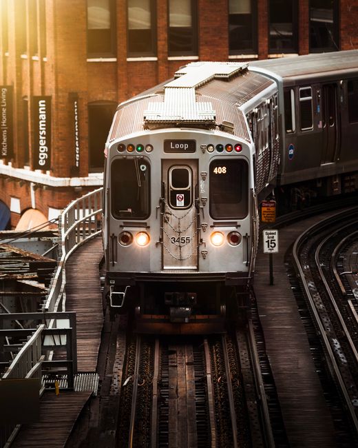 A Chicago L train navigates through the city on a wooden elevated track at sunset.