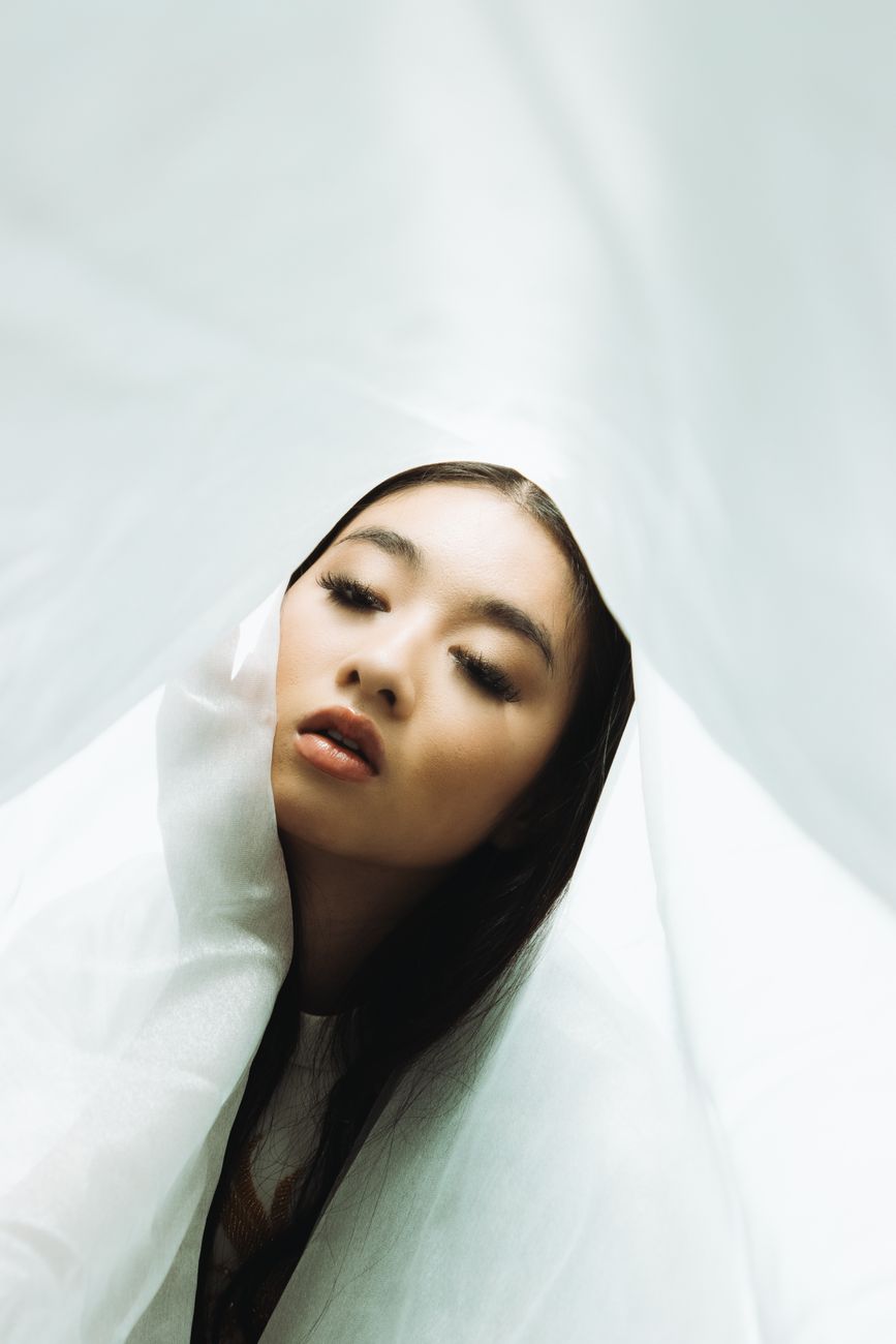 Artistic portrait of a woman wrapped in a flowing white veil, emphasizing elegance and grace.