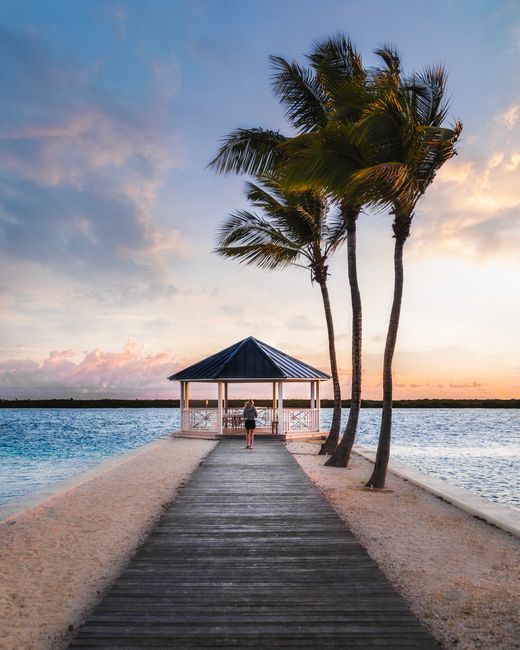 Relaxing tropical beach scene with a gazebo, palm trees, and serene sunset.
