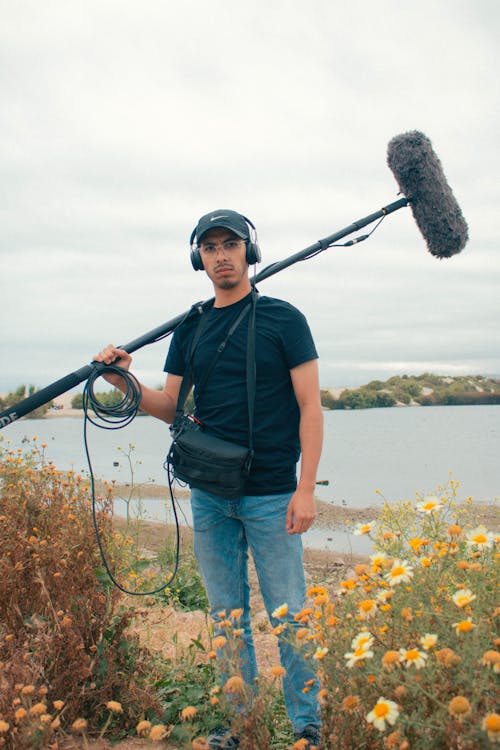 A man holding a microphone and camera in front of a lake