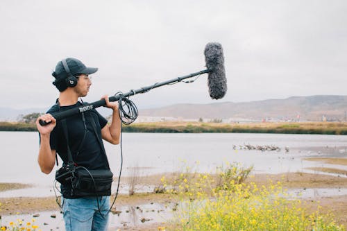 A man holding a microphone and camera near a lake