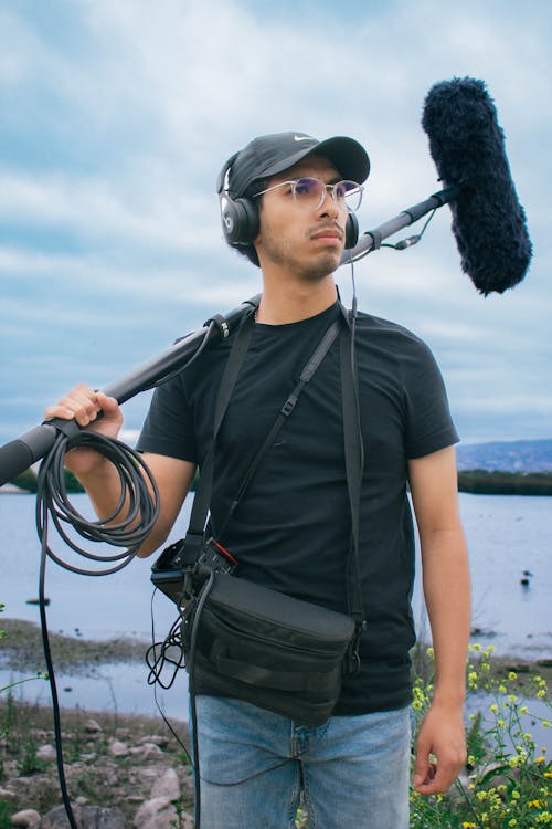 A man with headphones and a microphone stands by the water