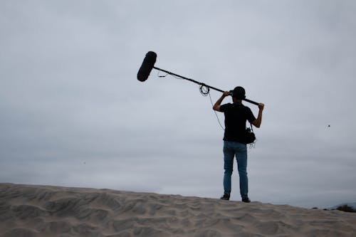 A person holding a camera on top of a sand dune