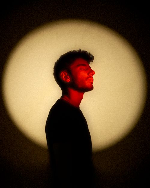 Free Profile of a man in dramatic yellow and red lighting, eyes closed, in a studio setting. Stock Photo
