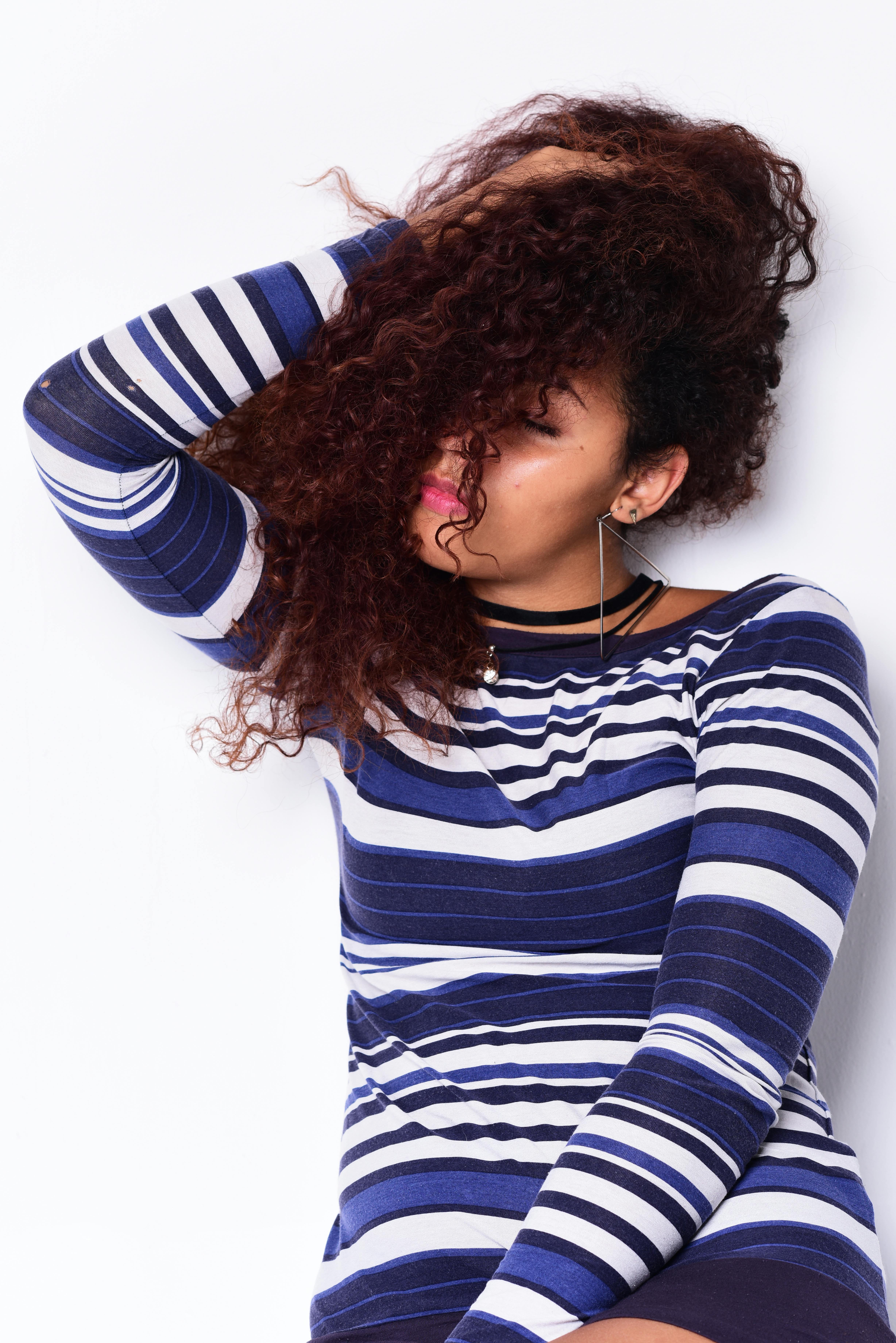 Stylish woman with curly hair poses in a navy striped dress against a white background.