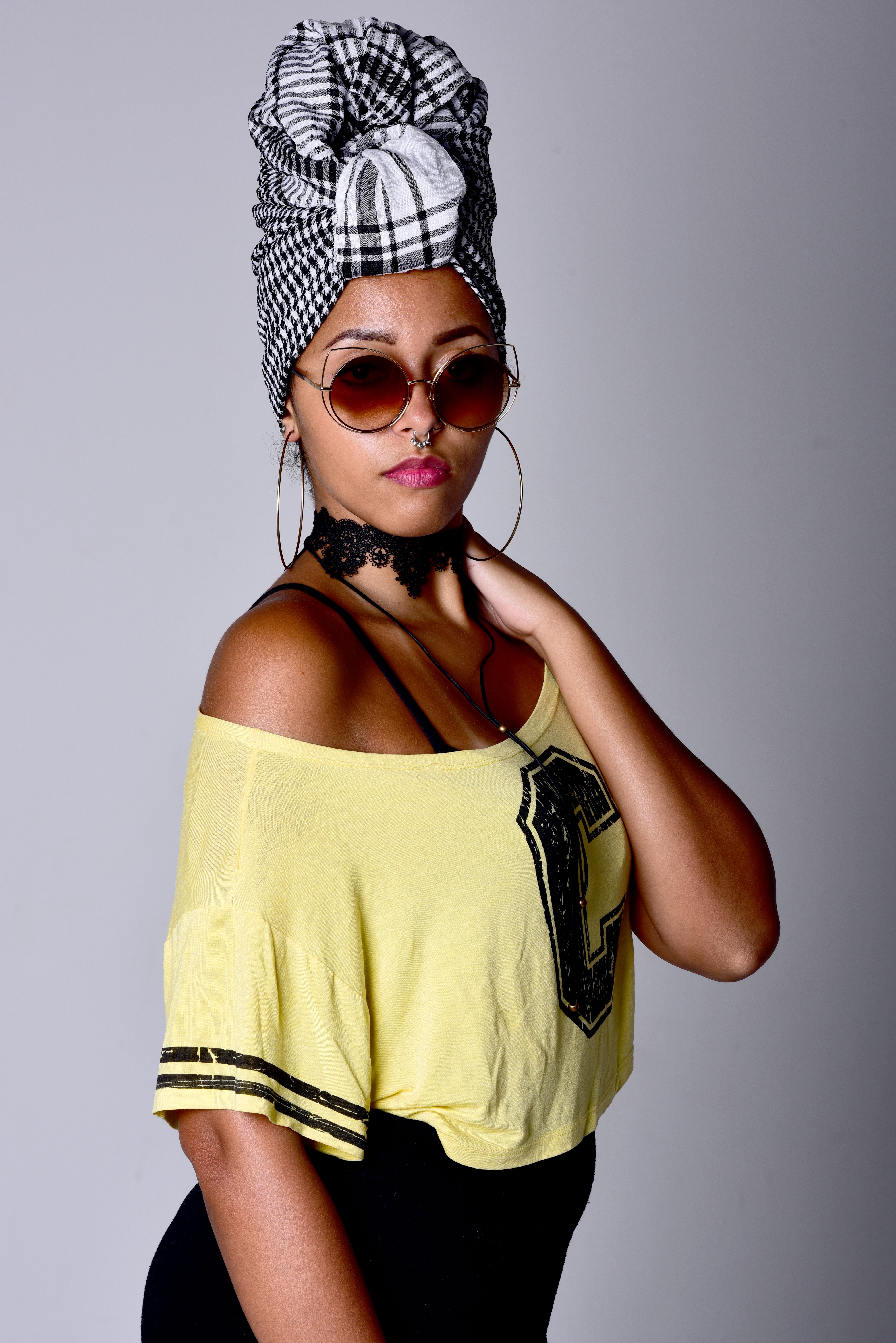 Stylish portrait of a woman in a headscarf, sunglasses, and yellow t-shirt indoors.