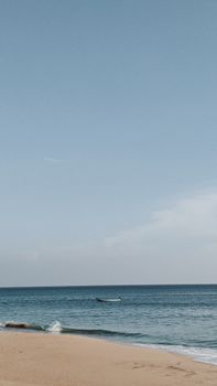 A peaceful beach scene with a distant boat on the calm sea under a clear sky.