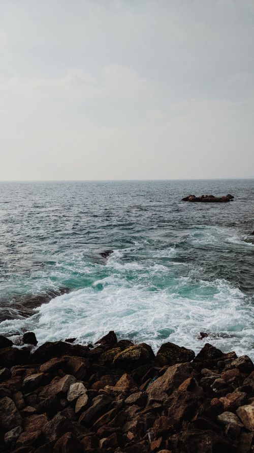 Free A stunning view of ocean waves crashing against a rugged rocky coastline under a moody sky. Stock Photo
