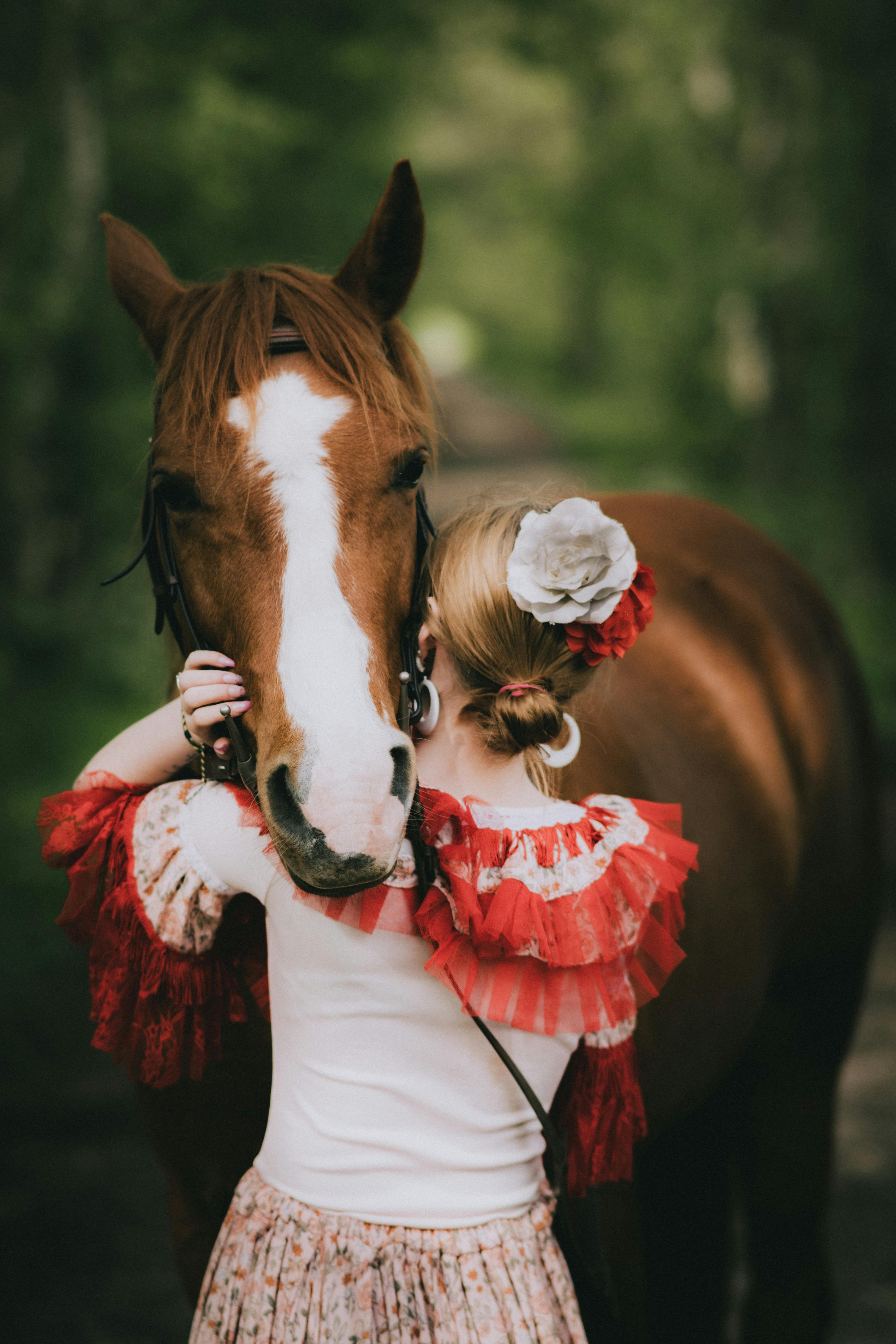 A woman in traditional clothing embraces a horse in a tranquil forest setting in Wallers, France.