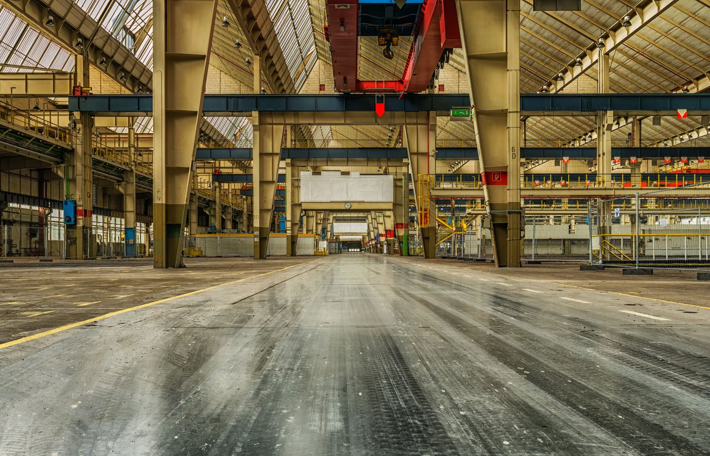 Wide view of an empty industrial warehouse with visible cranes and metal structures.