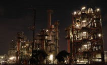 这张夜间照片展示了灯光明亮的工业设施，其复杂的钢结构和机械清晰可见