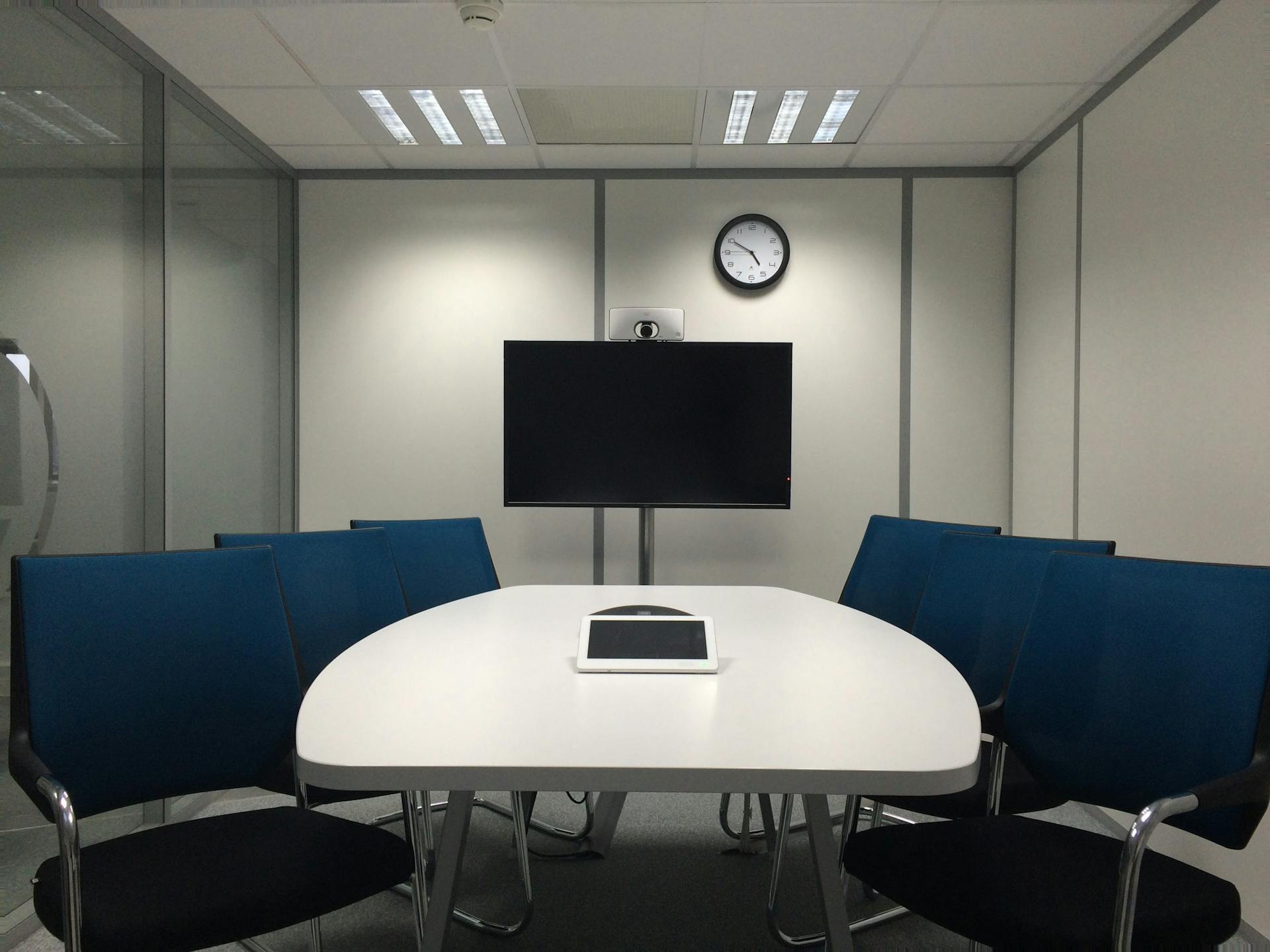 Sleek conference room with a table, chairs, TV, and video conferencing equipment.