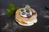 蓝莓煎饼的特写镜头中，上面点缀着奶油、薄荷和糖粉