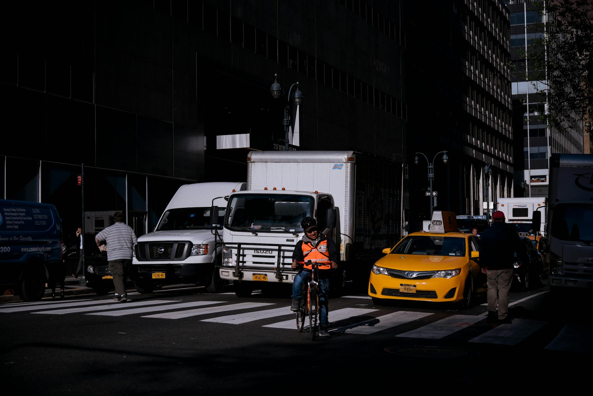 Cyclist navigates busy street in New York City traffic, surrounded by vehicles and buildings.