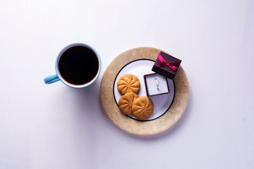 Cooked Bread Beside Bridal Ring on Box Beside Ceramic Mug Filled With Black Liquid