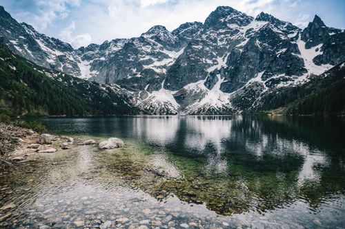 Free Majestic snow-capped mountains reflecting in a serene alpine lake with clear skies. Stock Photo