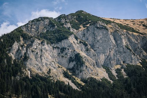 Free A scenic view of a tall rocky mountain with green foliage in the summer. Stock Photo