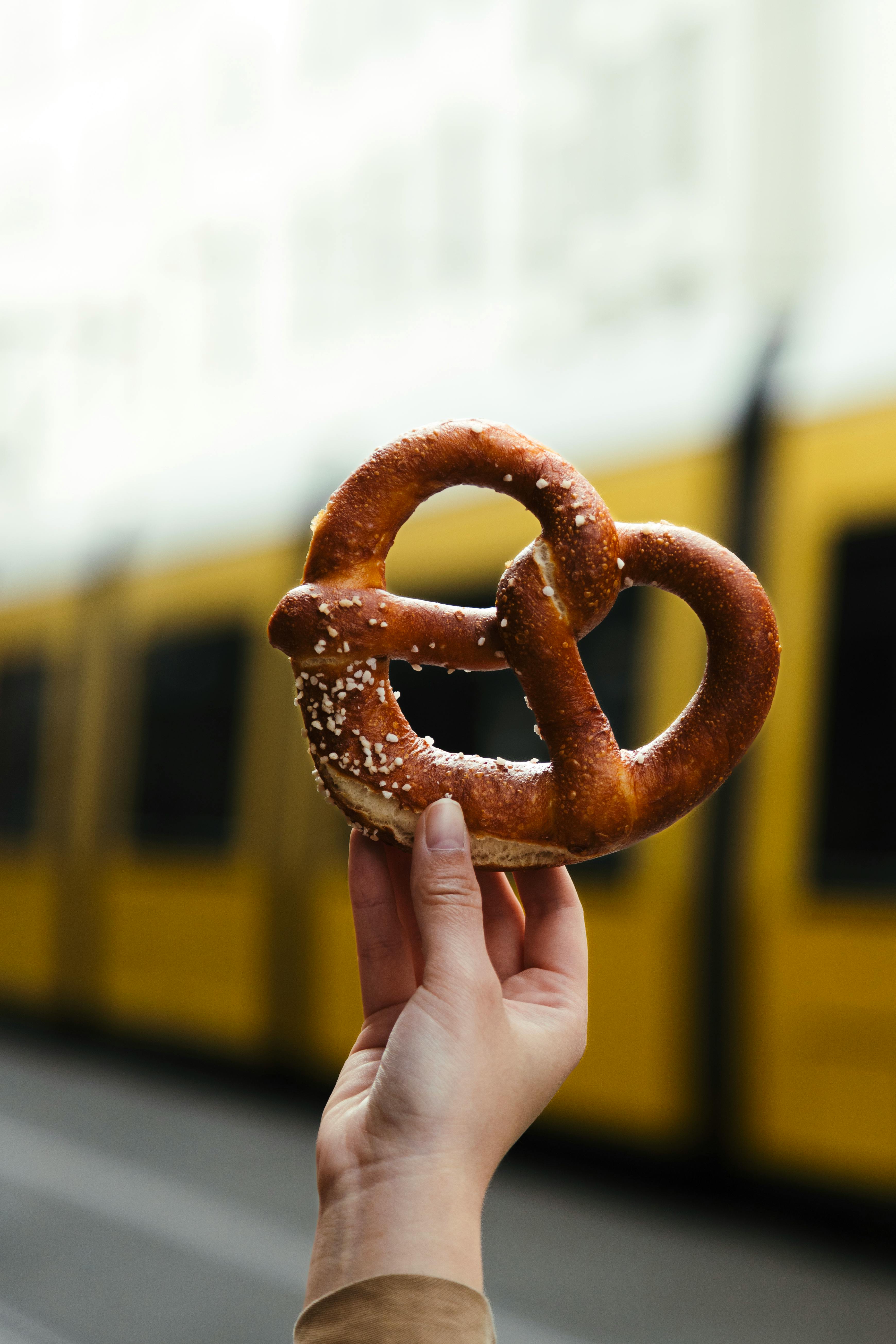Close-up of a hand holding a pretzel against a blurred Berlin tram background.