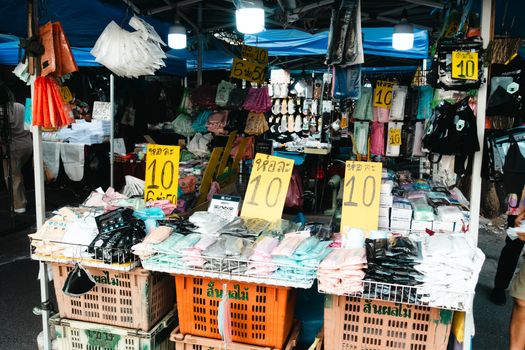 Colorful street market with clothing stalls and sale signs, vibrant and bustling.