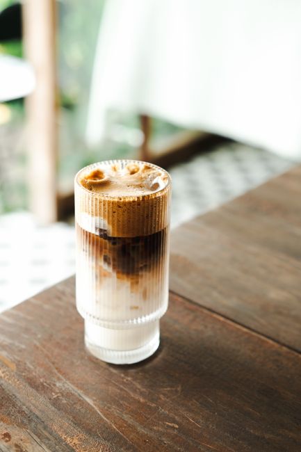 Iced latte served in a glass placed on a wooden table, captured in Đà Lạt, Vietnam.