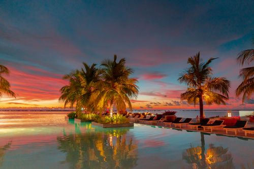 Free Luxurious infinity pool with palm trees at sunset, creating a tropical paradise vibe. Stock Photo
