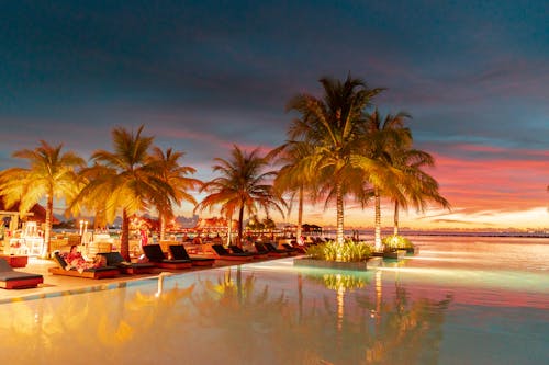 ropical Paradise at Dusk: Experience the stunning blend of fiery skies and serene waters at a luxurious Maldives resort, where palm trees are silhouetted against the vibrant sunset, and tr...