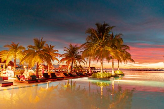 A serene resort with palm trees and loungers by the ocean under a colorful sunset sky.