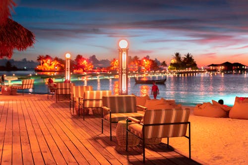ropical Paradise at Dusk: Experience the stunning blend of fiery skies and serene waters at a luxurious Maldives resort, where palm trees are silhouetted against the vibrant sunset, and tr...