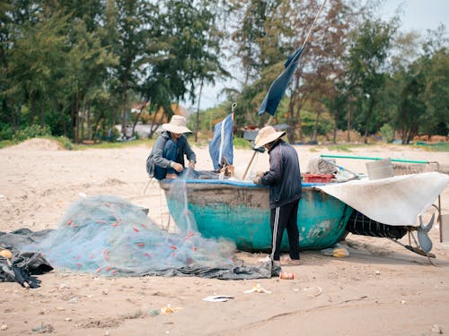 Two people are working on a boat on the beach