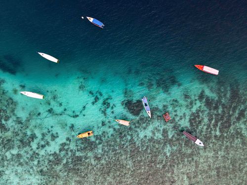 Free Aerial shot of colorful boats floating over clear waters in Kecamatan Pemenang, Indonesia. Stock Photo