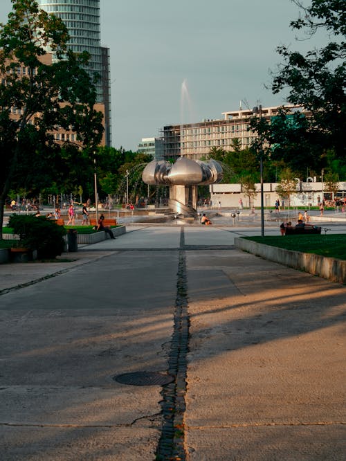 A man is walking down a sidewalk with a fountain in the background