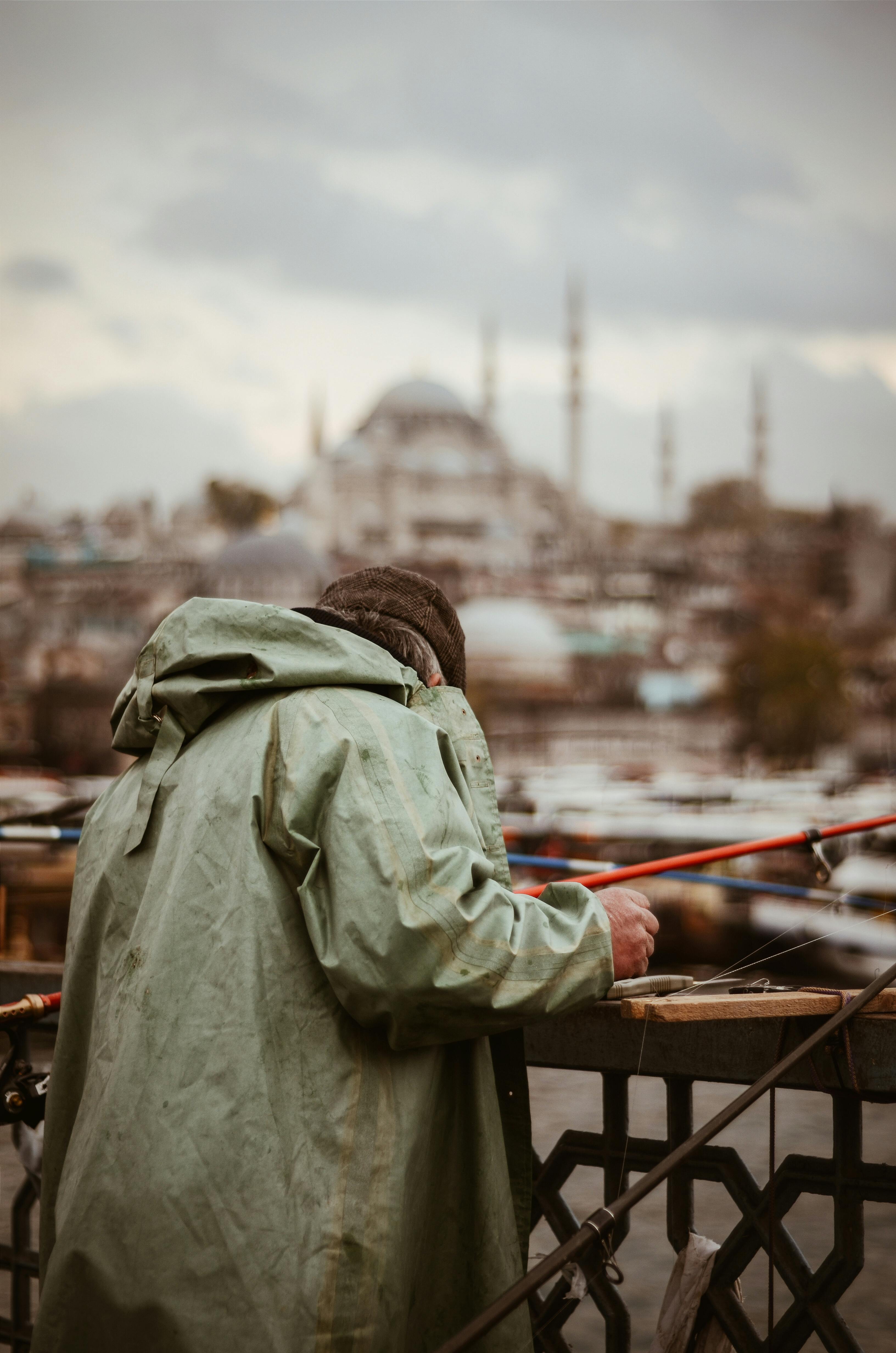 在伊斯坦布尔标志性的加拉塔桥上，一名穿着冬季夹克的渔民正在钓鱼，背景是一座清真寺
