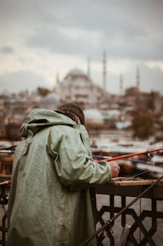 在伊斯坦布尔标志性的加拉塔桥上，一名穿着冬季夹克的渔民正在钓鱼，背景是一座清真寺