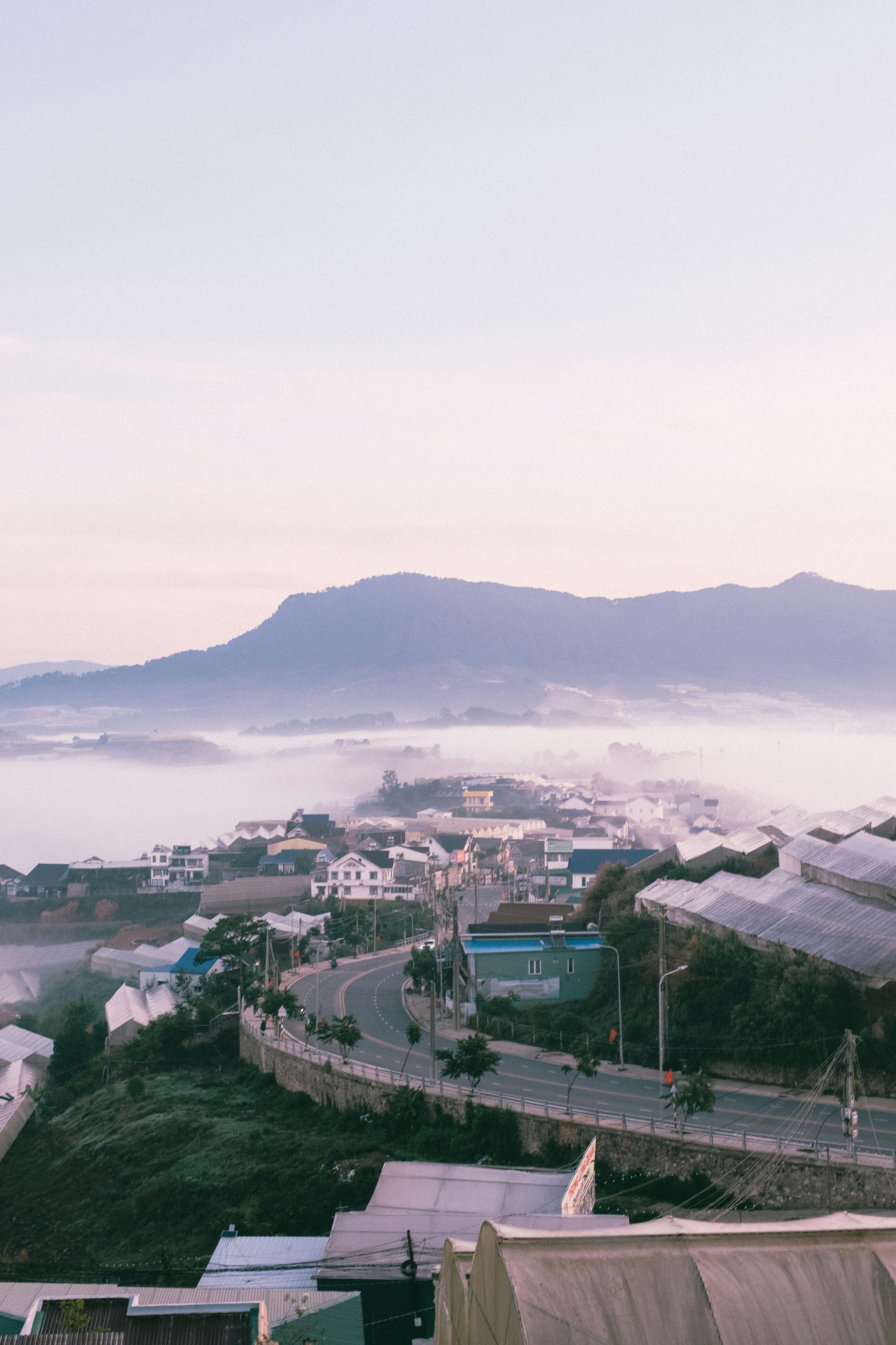 Aerial view of a mountain town enveloped in morning fog, under a serene sunrise.