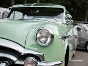 在户外车展上，一辆经典绿色汽车的特写照片展示了其前灯和镀铬细节