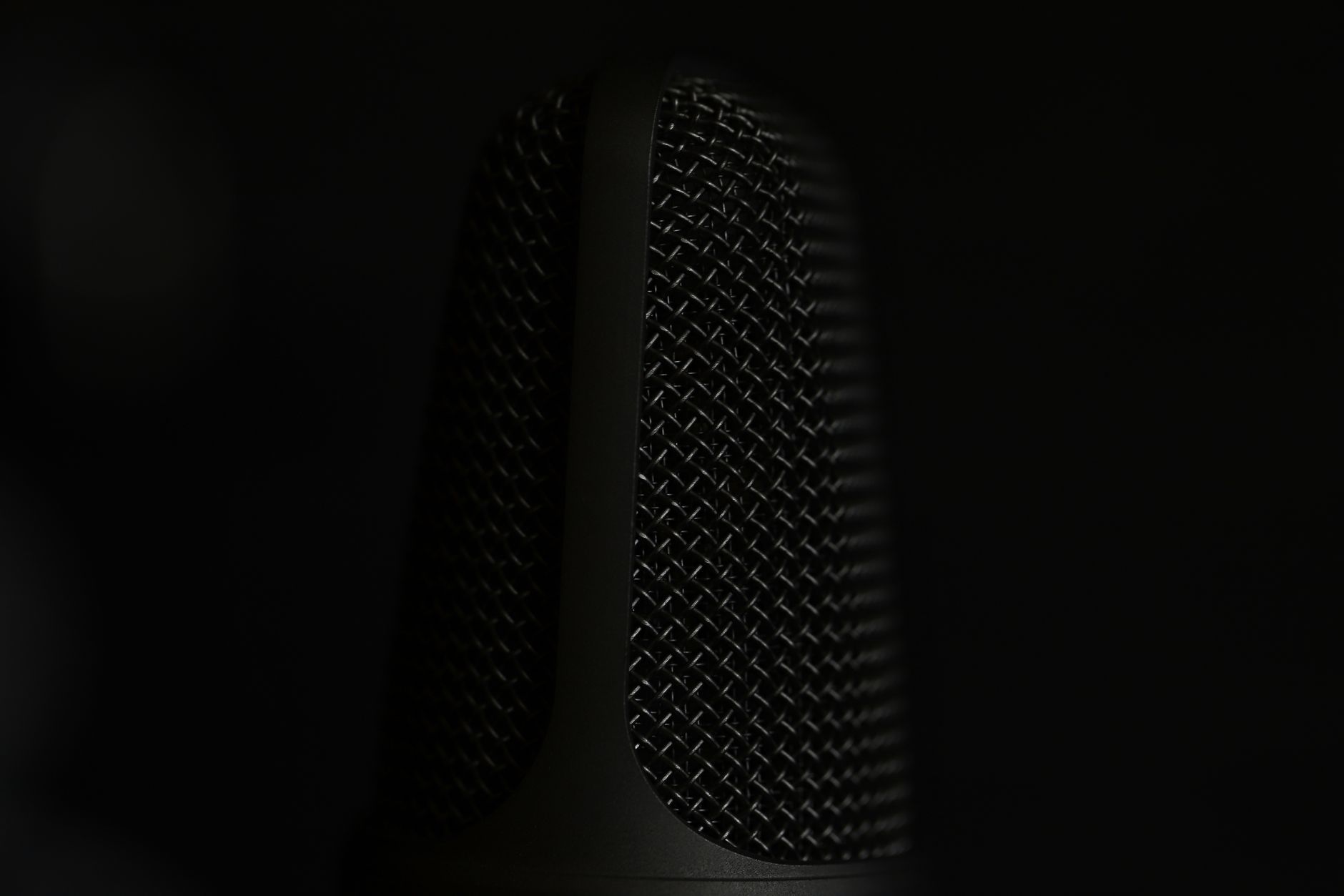 A detailed macro shot of a microphone in a studio setting with a dark background.